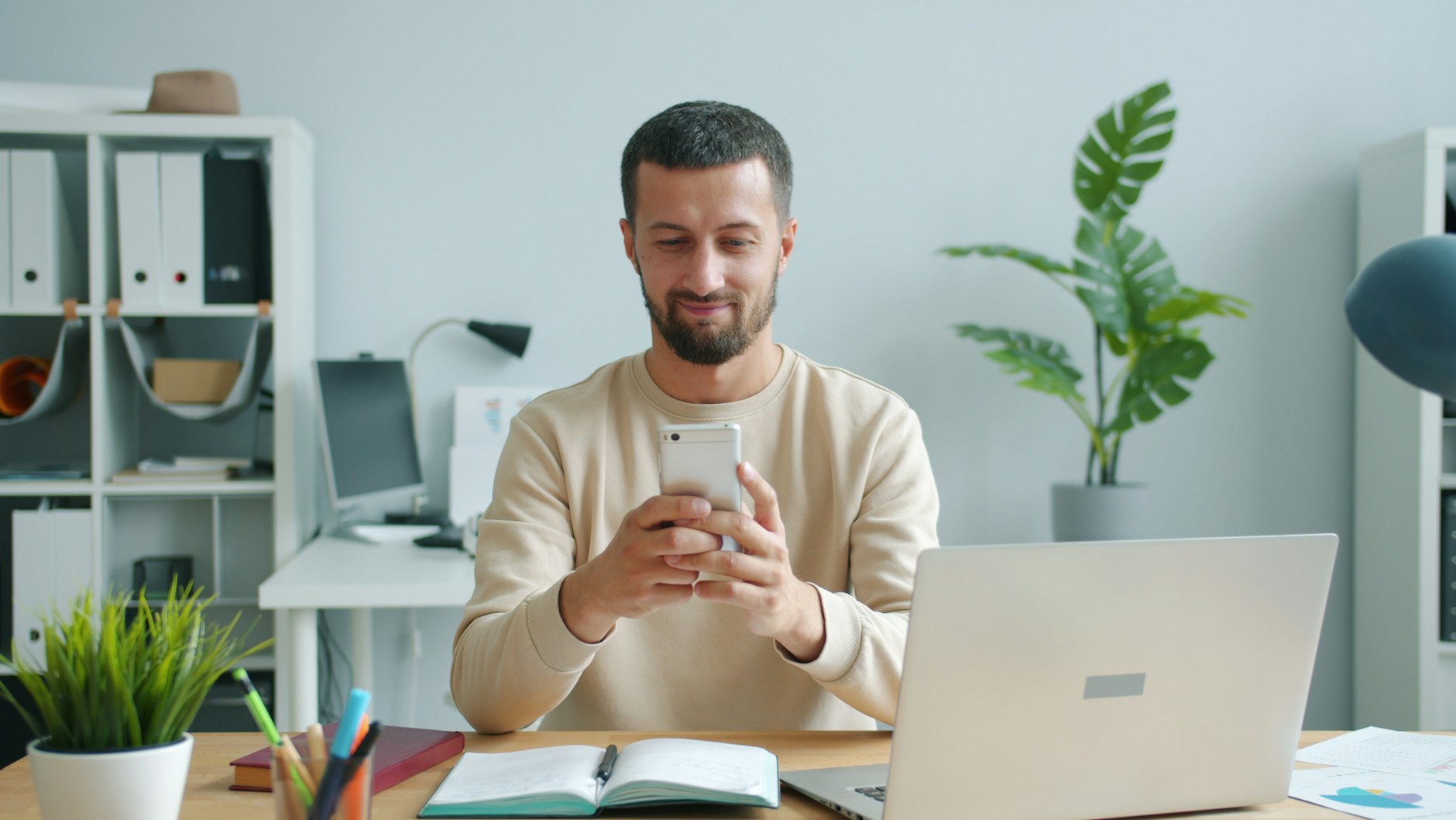 personne en tenue de bureau qui consulte un smartphone à son poste de travail, ordinateur portable ouvert