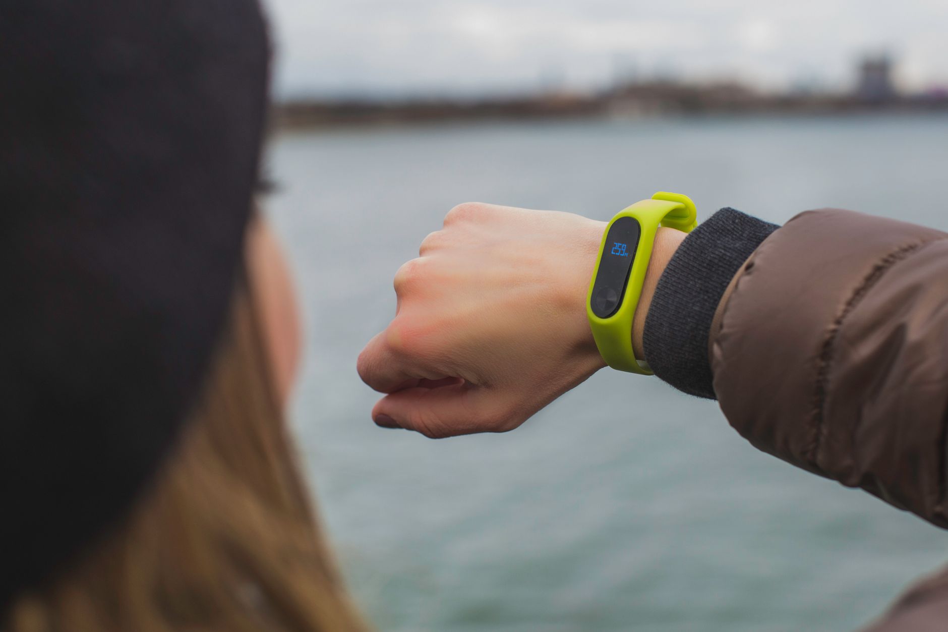 bracelet connecté vert porté au poignet, avec un petit écran allongé, devant un plan d'eau