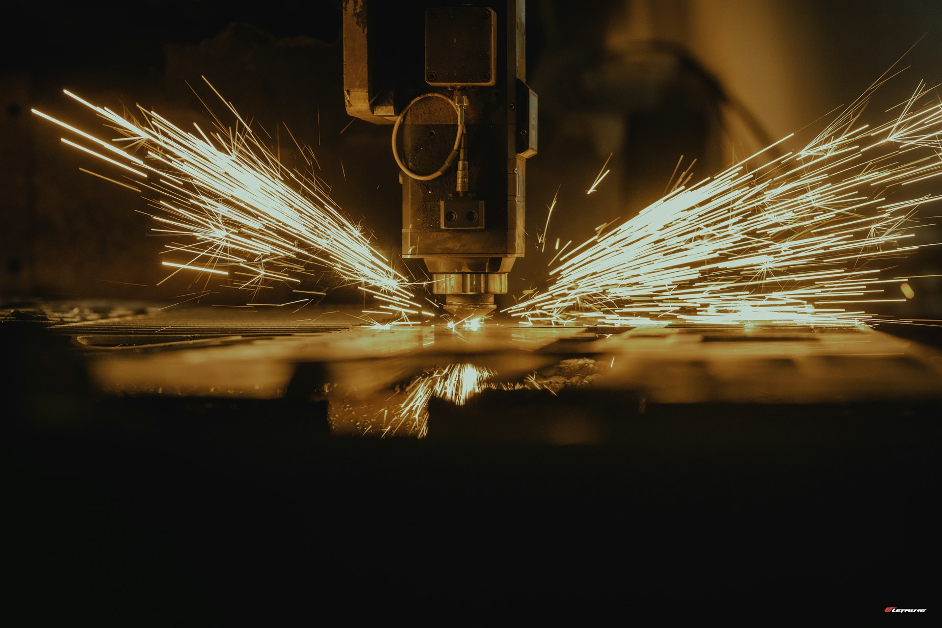 étincelles projetées par une machine de découpe laser qui tranche une pièce métallique, dans un atelier industriel