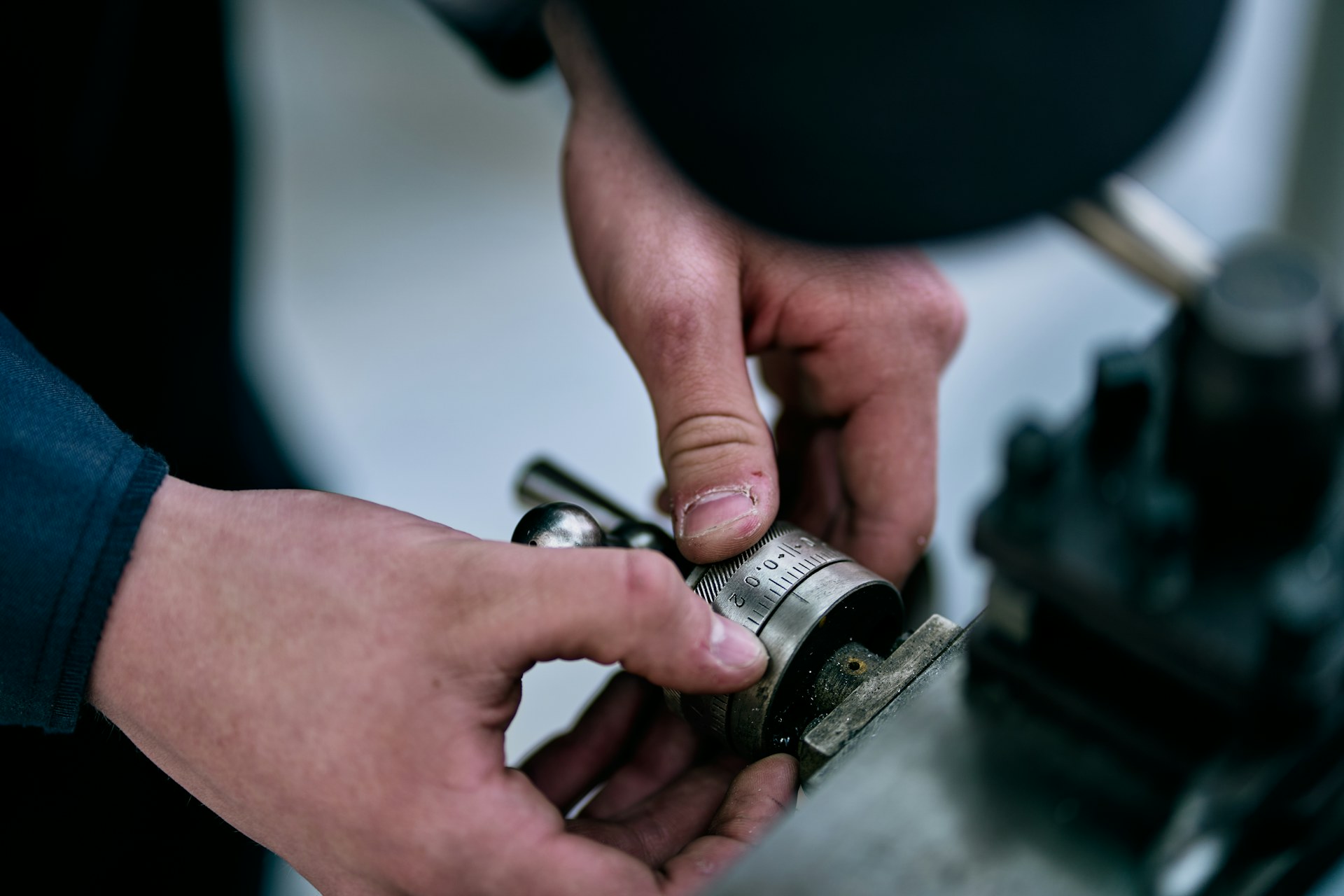 mains qui règlent un instrument de mesure de précision sur une pièce mécanique, dans un atelier industriel